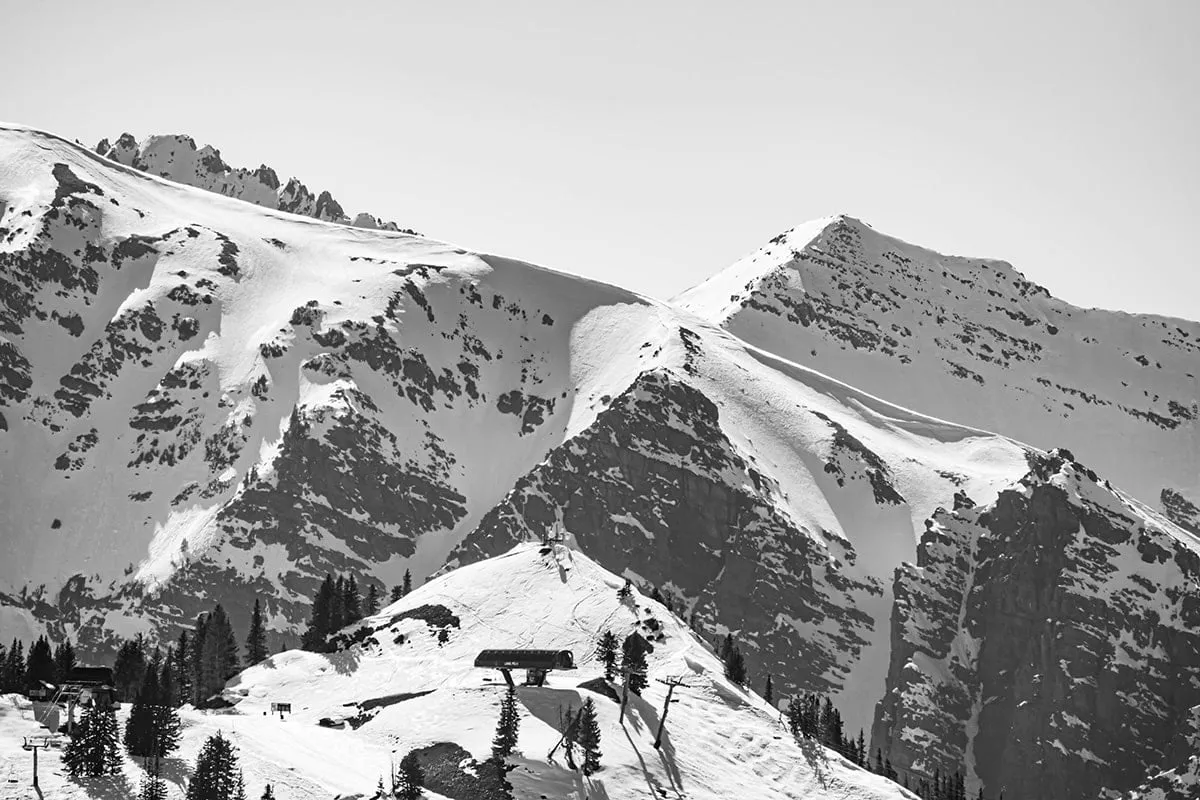 Black-and-white view of snowy peaks above a ski slope with a small lift hut and scattered pines