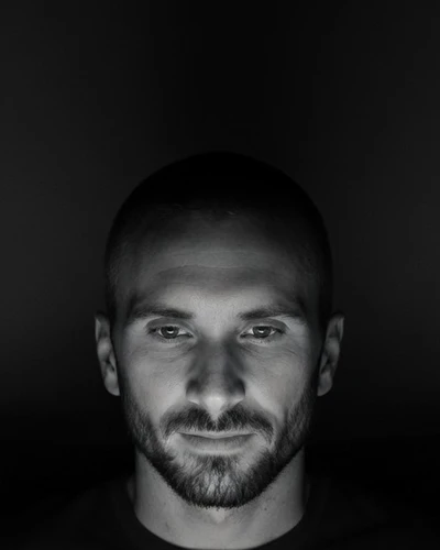 Black-and-white portrait of Kyle Rutten, short hair and a beard, his face lit by a laptop screen in a dark room