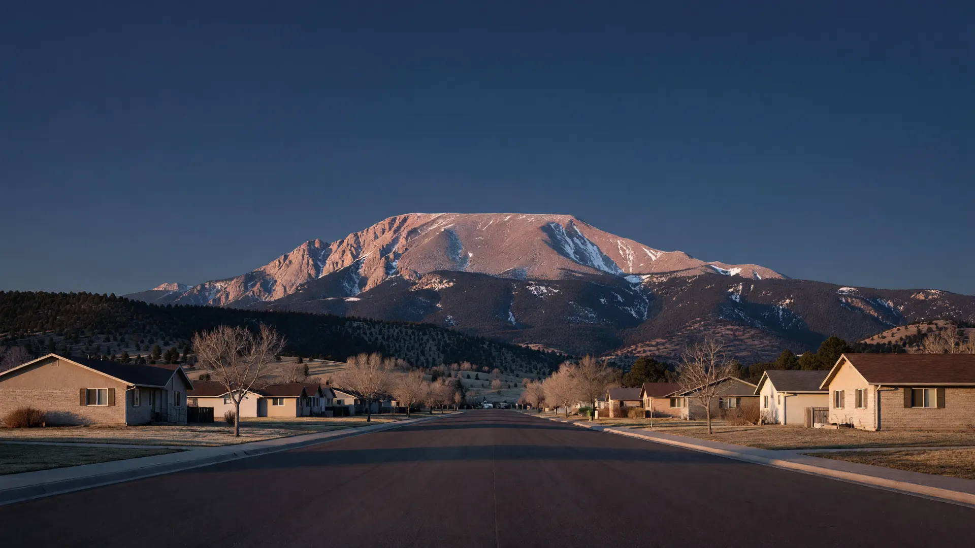 A quiet neighborhood street at golden hour, running west toward Pikes Peak