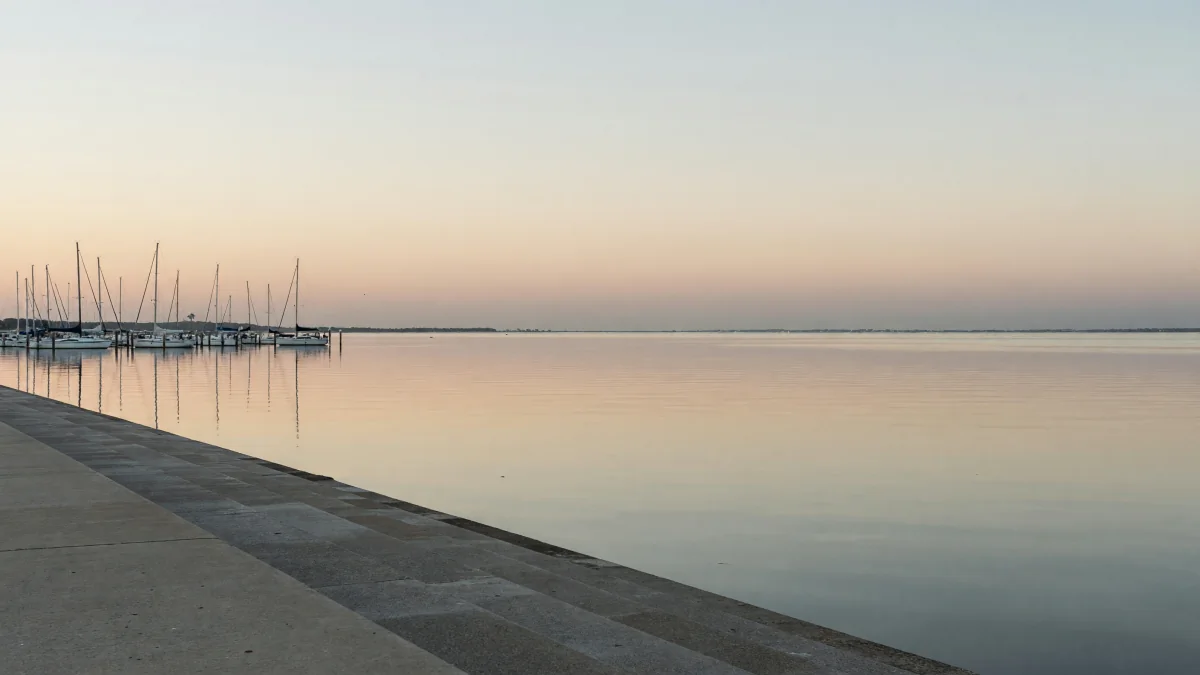 Sailboats moored in a marina on calm Corpus Christi Bay at first light, seen from the stepped concrete bayfront seawall