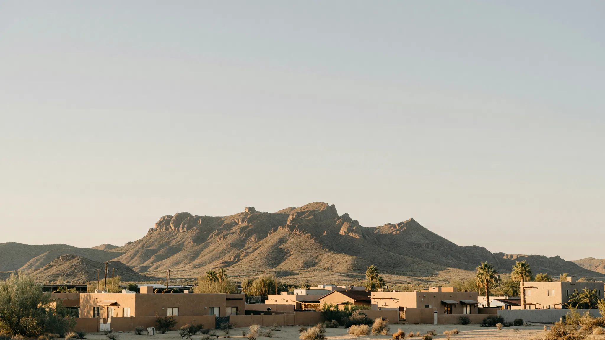 The Franklin Mountains in late-afternoon light above low stucco rooftops and palm trees in El Paso