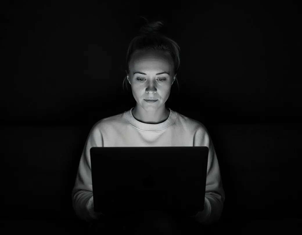 Katie Rutten of Bullfinch working on a laptop in a dark room, in black and white