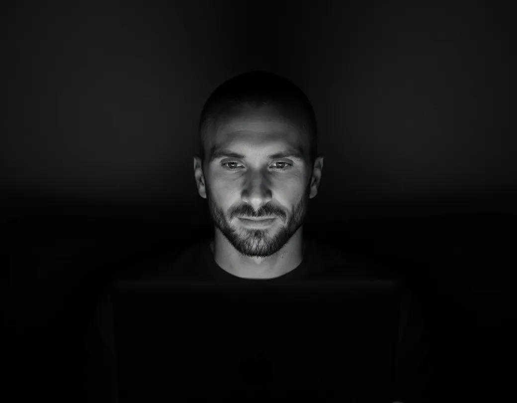 Kyle Rutten of Bullfinch, lit by his laptop screen in a dark room, in black and white