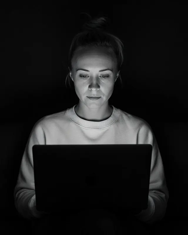 Katie Rutten, who runs each Bullfinch project and account, at a laptop in a dark room, her face lit by the screen