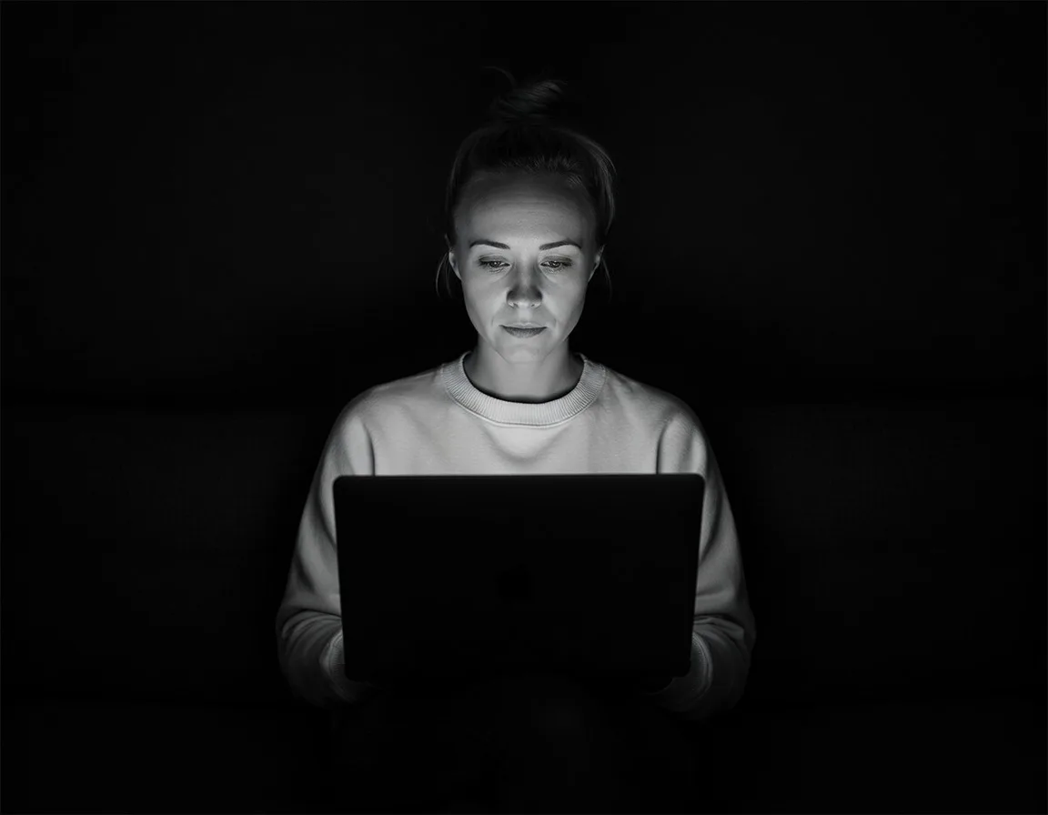 Katie Rutten in black and white, in a pale sweater, reading her laptop screen