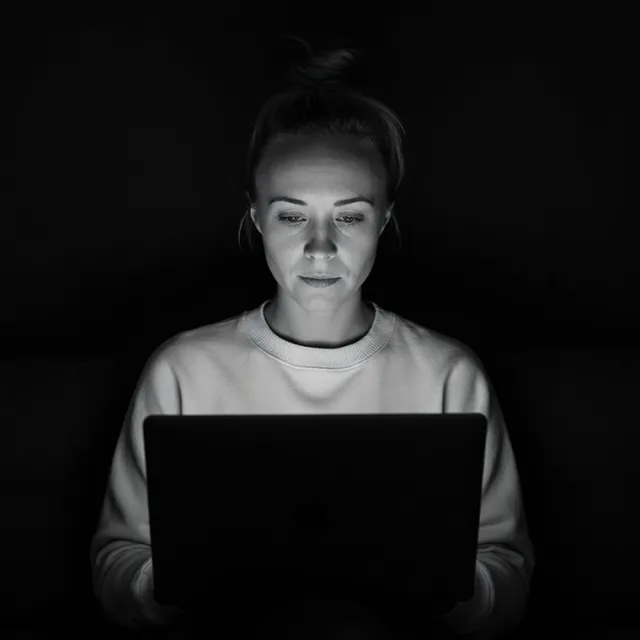 Katie Rutten, black-and-white portrait, working on a laptop in a dark room