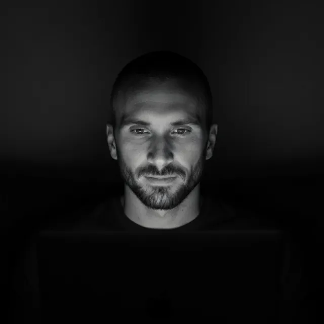 Kyle Rutten, black-and-white portrait, his face lit by a laptop screen in a dark room