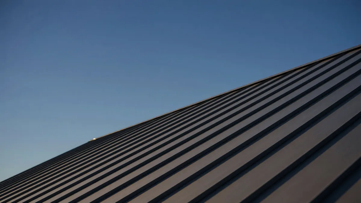 Low view along a new dark standing-seam metal roof, its raised seams running up the slope against a clear evening sky