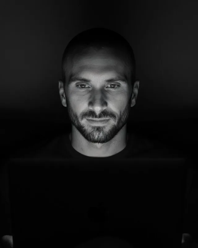 Kyle Rutten, who designs and builds Bullfinch sites, lit by a laptop screen in a dark room