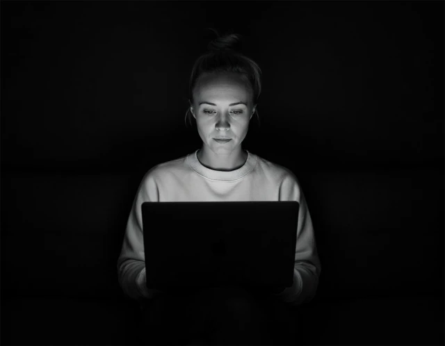 Katie Rutten in a light sweater, working at a laptop in a dark room.