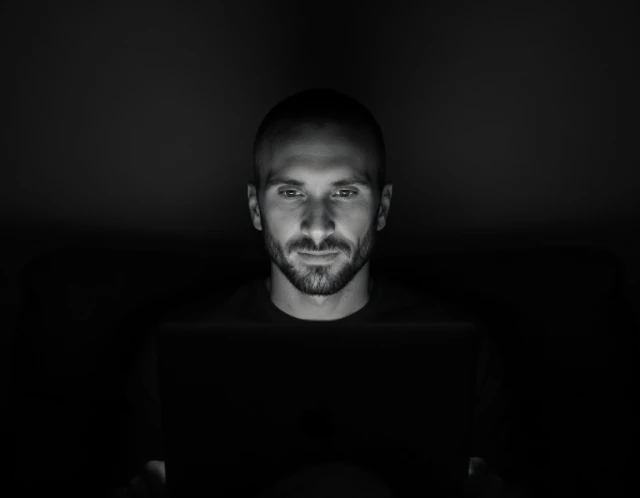 Kyle Rutten working at a laptop, his face lit by the screen in a dark room.