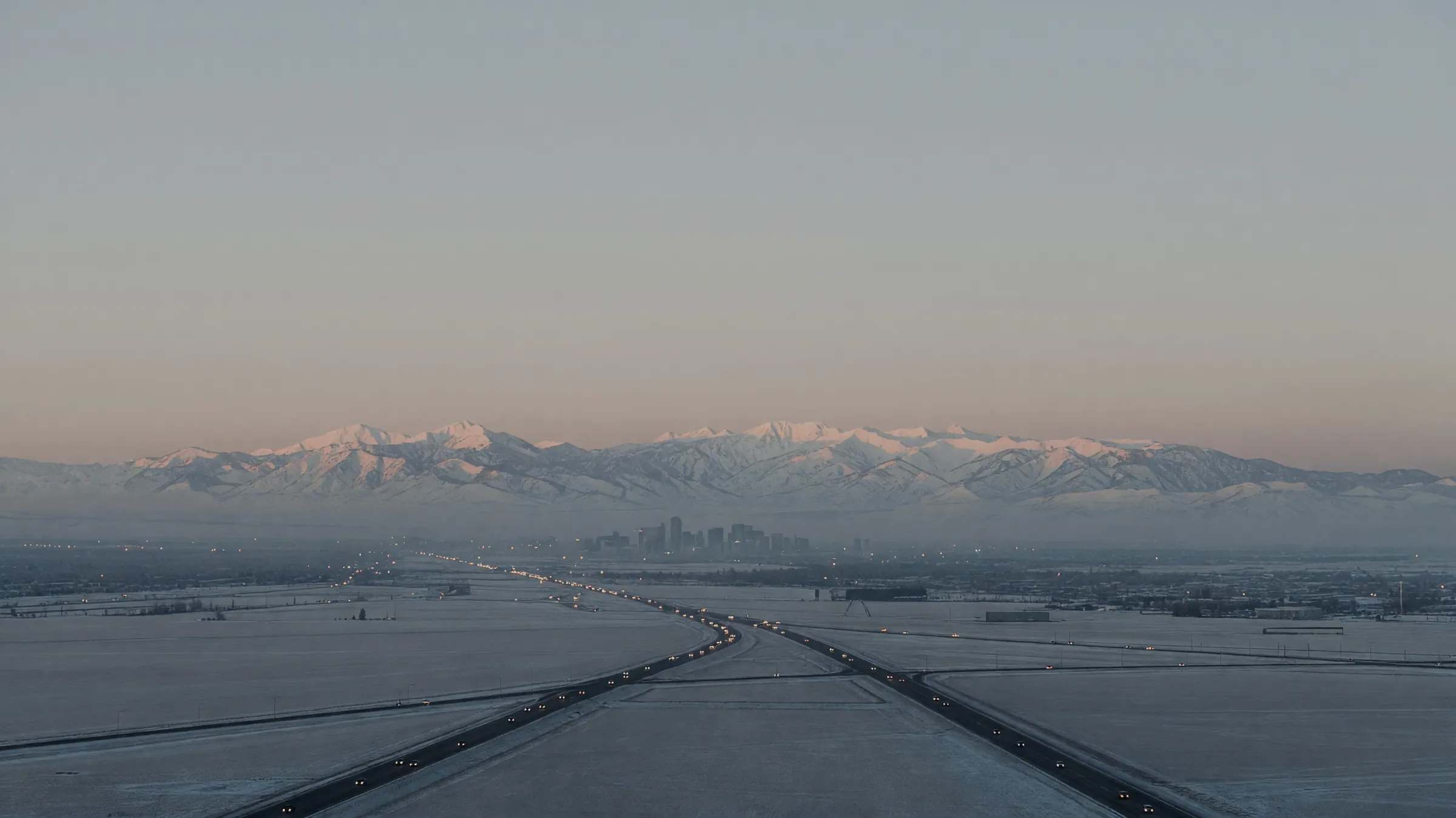 Dawn over the Salt Lake valley: headlight streams flow toward downtown towers under the snow-topped Wasatch.