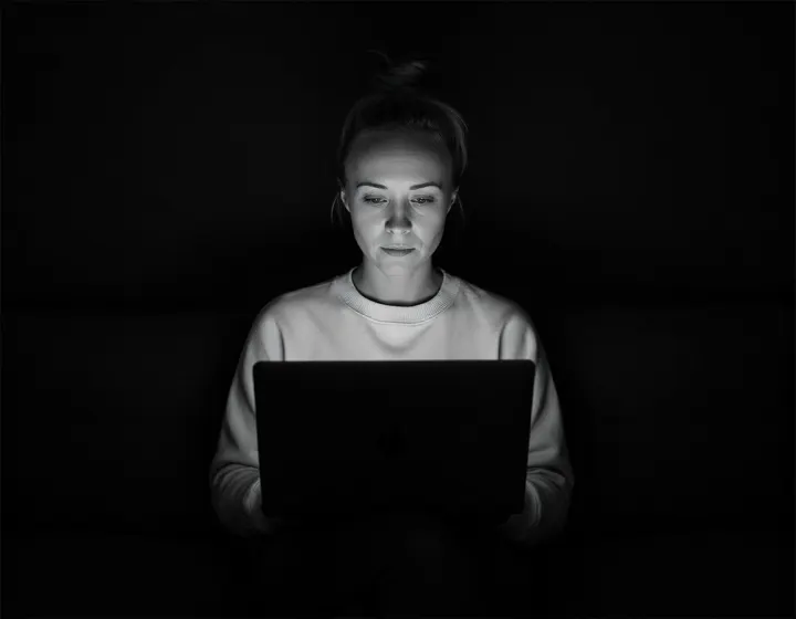 Katie Rutten working on a laptop in a dark room, in a black and white portrait