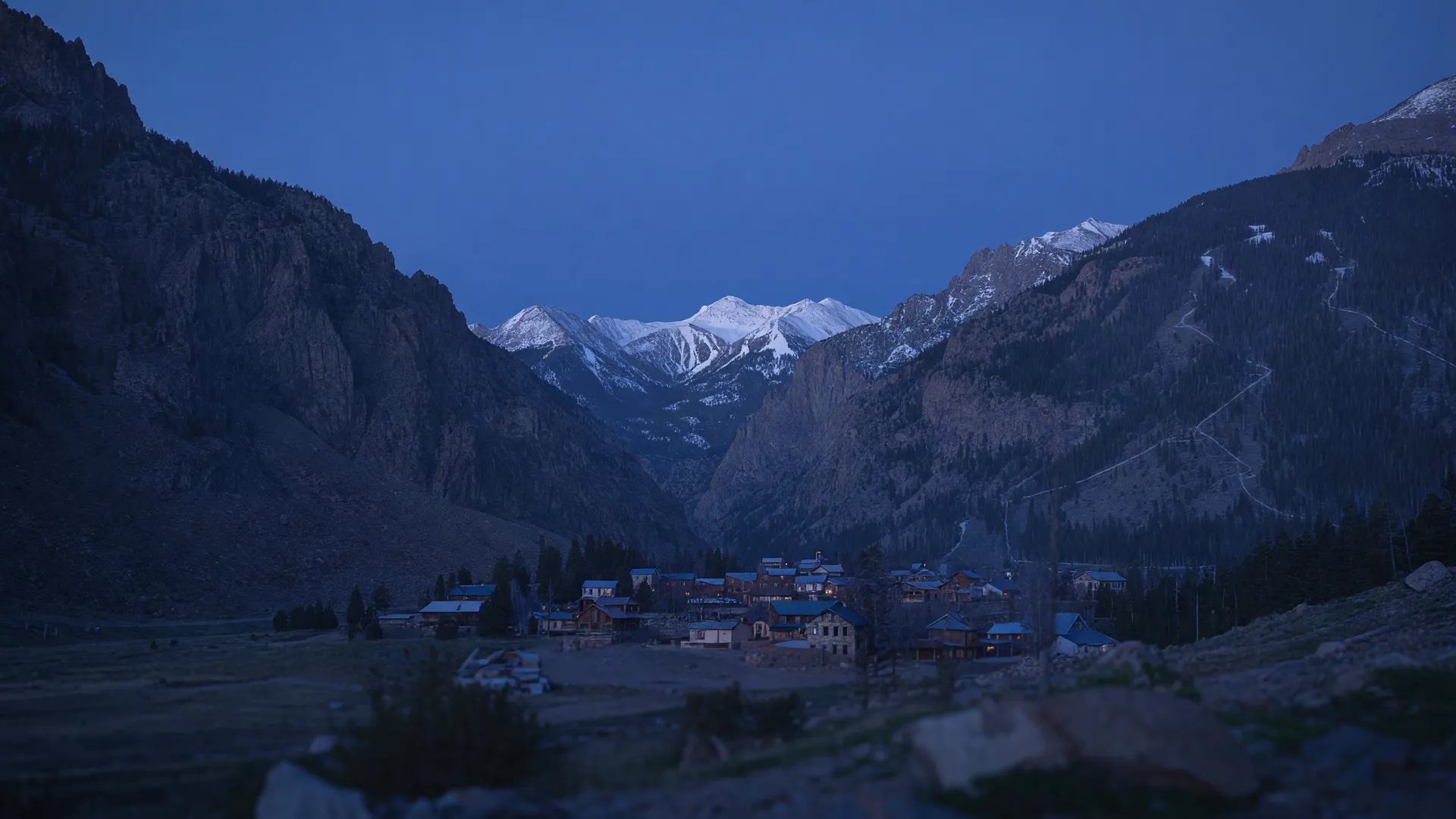 Illustrative scene: a small mountain town at the end of a steep box canyon at dusk, snow on the peaks, a few windows lit.