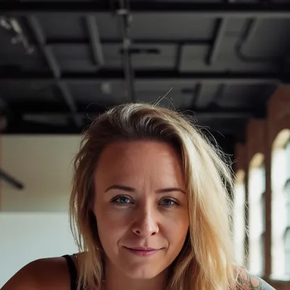 Katie Rutten, shoulder-length blonde hair, smiling slightly at the camera in a bright brick workspace.