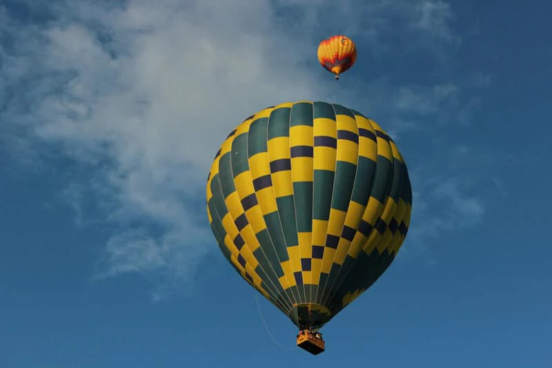 Two hot-air balloons in a blue sky: a large yellow and green checked one close overhead, a smaller orange and red one above