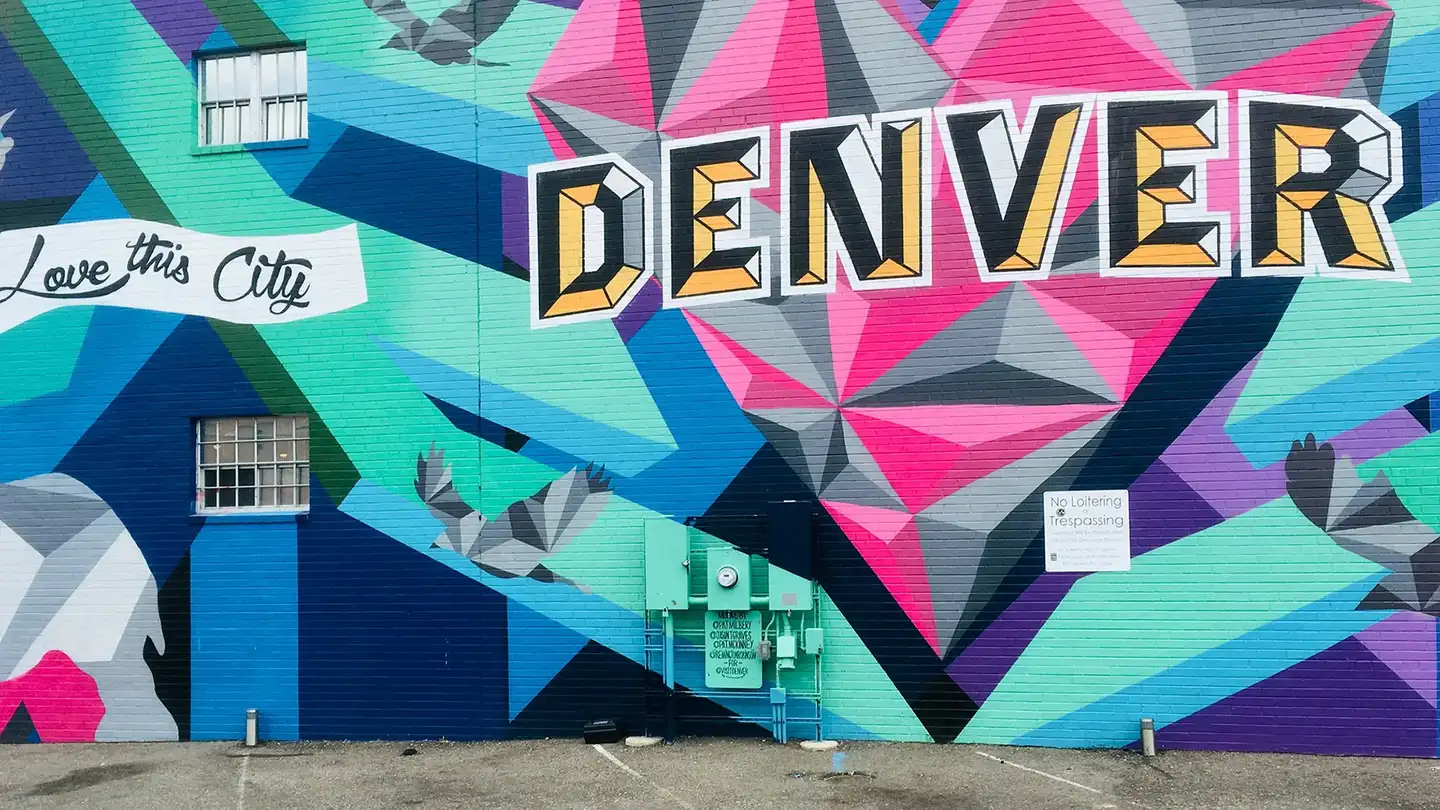 Street mural on a Denver brick wall: DENVER in black and gold letters over a pink diamond and teal and purple stripes