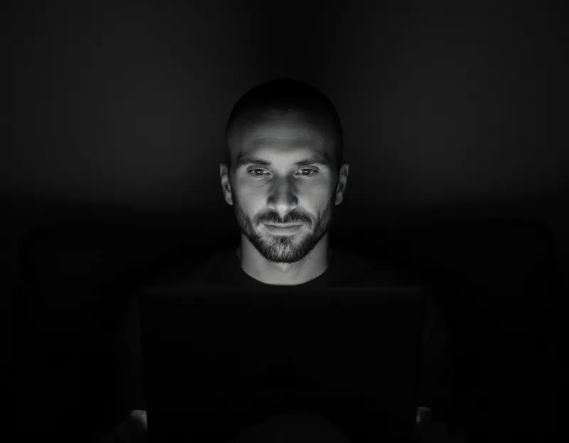 Kyle of Bullfinch, short hair and a beard, his face lit by a laptop screen in a dark room