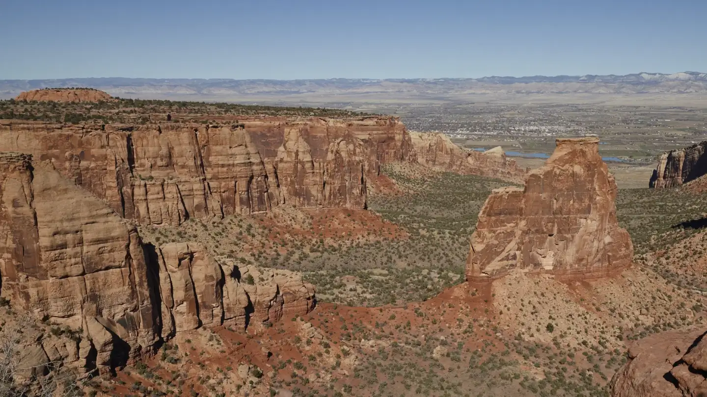 Independence Monument, a red sandstone tower in Colorado National Monument, with Grand Junction and the Book Cliffs behind