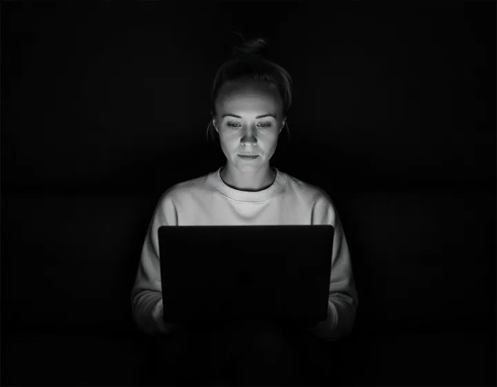 Katie Rutten, who runs your project and account, lit by the glow of her laptop in a dark room, black and white.